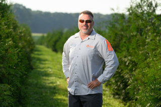 Ken Corrin of Rolling Fields Tree Farm standing in a field of Green Giant Arborvitae with hands on hips